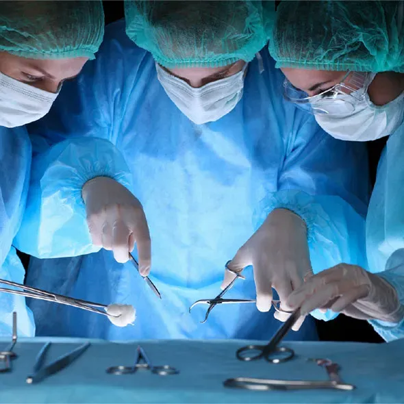 Three surgeons holding operating equipment standing over a tray of equipment wearing surgical masks and gowns
